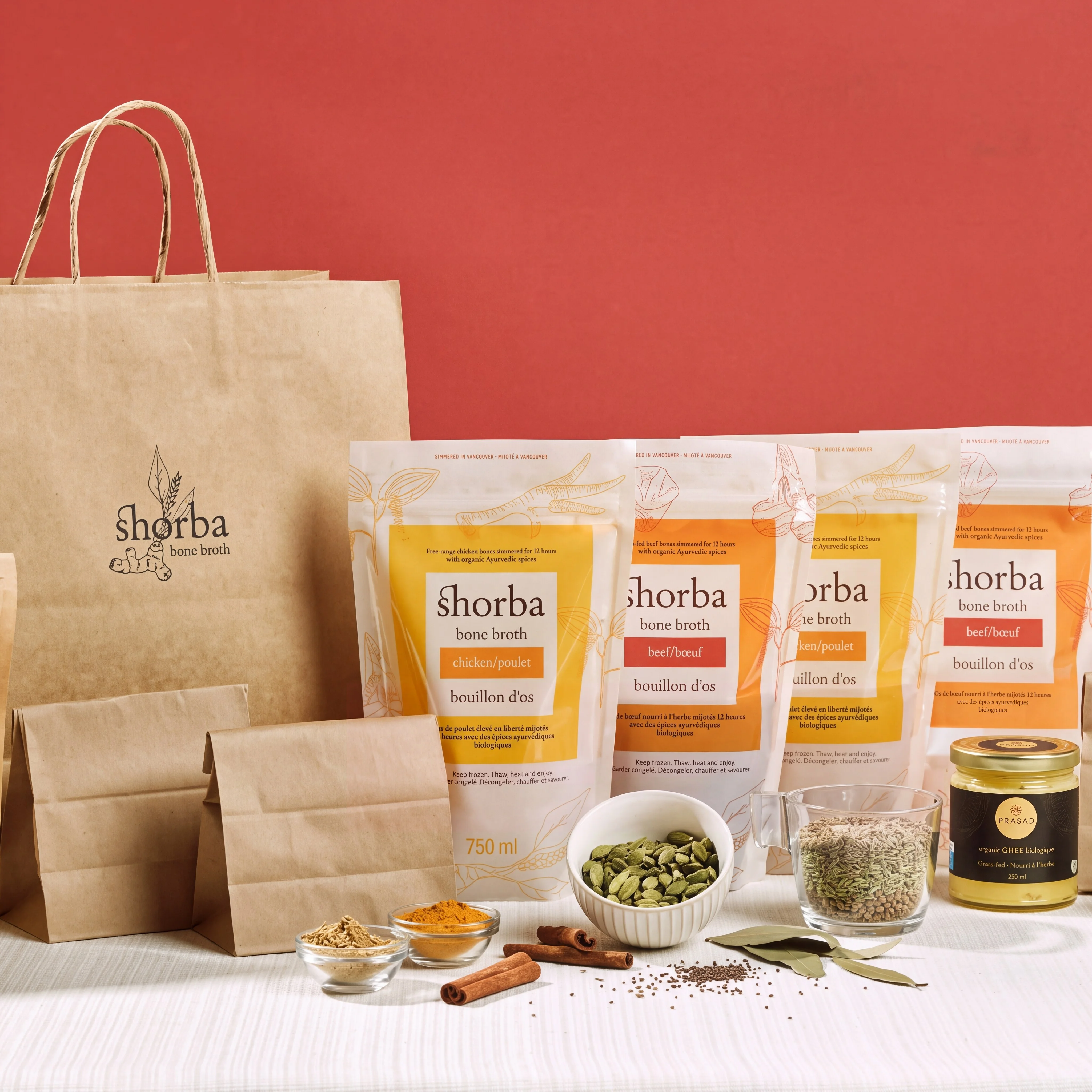 Shorba bone broth pouches beside a paper bag, bowls of Ayurvedic spices and cinnamon sticks