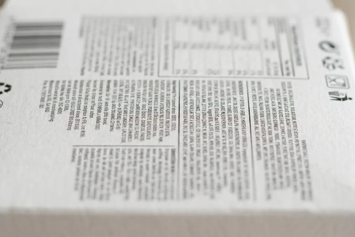 Close-up of a food product's information panel on white packaging, showing the detailed back label with text blocks representing the ingredient statement, nutrition facts, and allergen declaration grouped together
